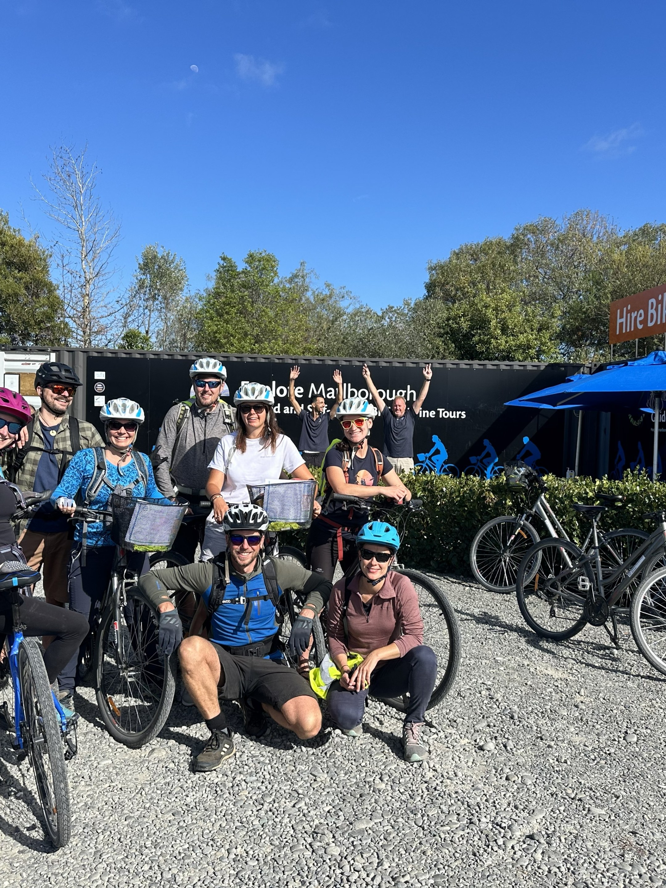Group of cyclists with helmets posing in front of a Explore Marlborough a bike hire shop.