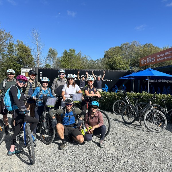 Group of cyclists with helmets posing in front of a Explore Marlborough a bike hire shop.