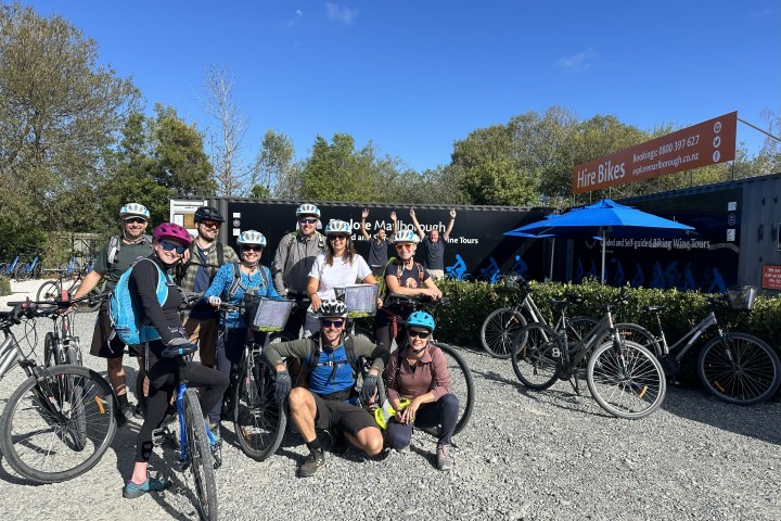 Group of cyclists with helmets posing in front of a Explore Marlborough a bike hire shop.
