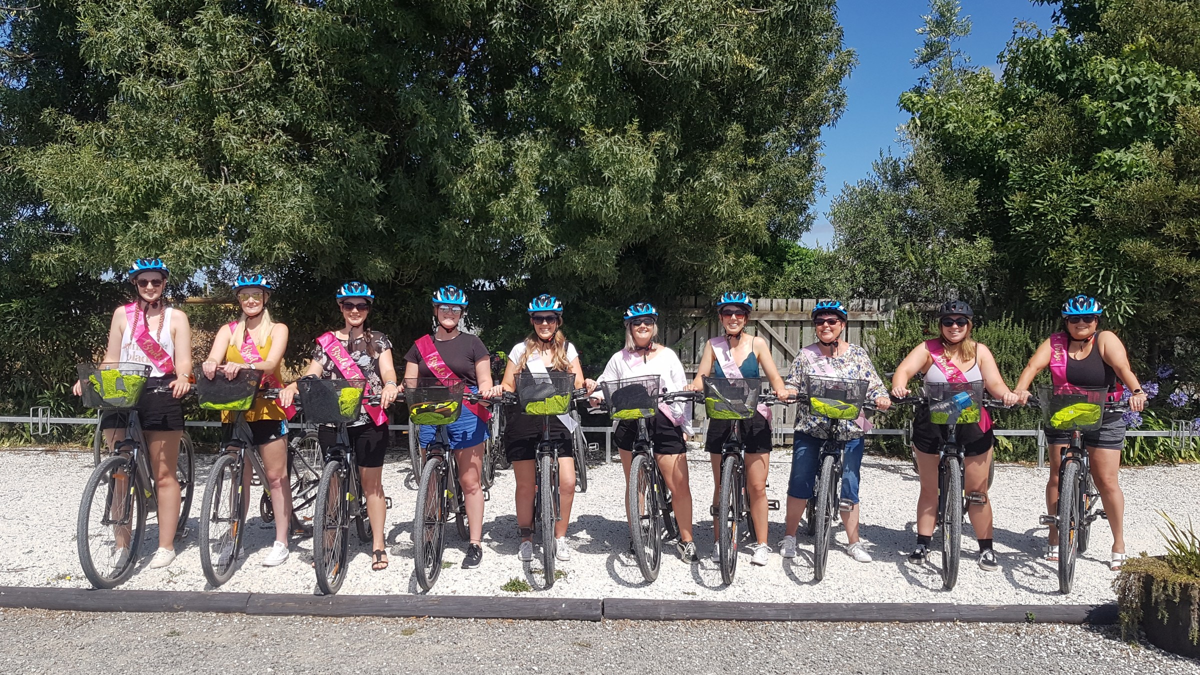 Group of people with bikes and blue helmets, standing outdoors on a sunny day.
