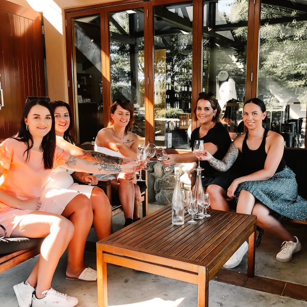 Five women sitting outside, toasting with glasses in a relaxed setting.