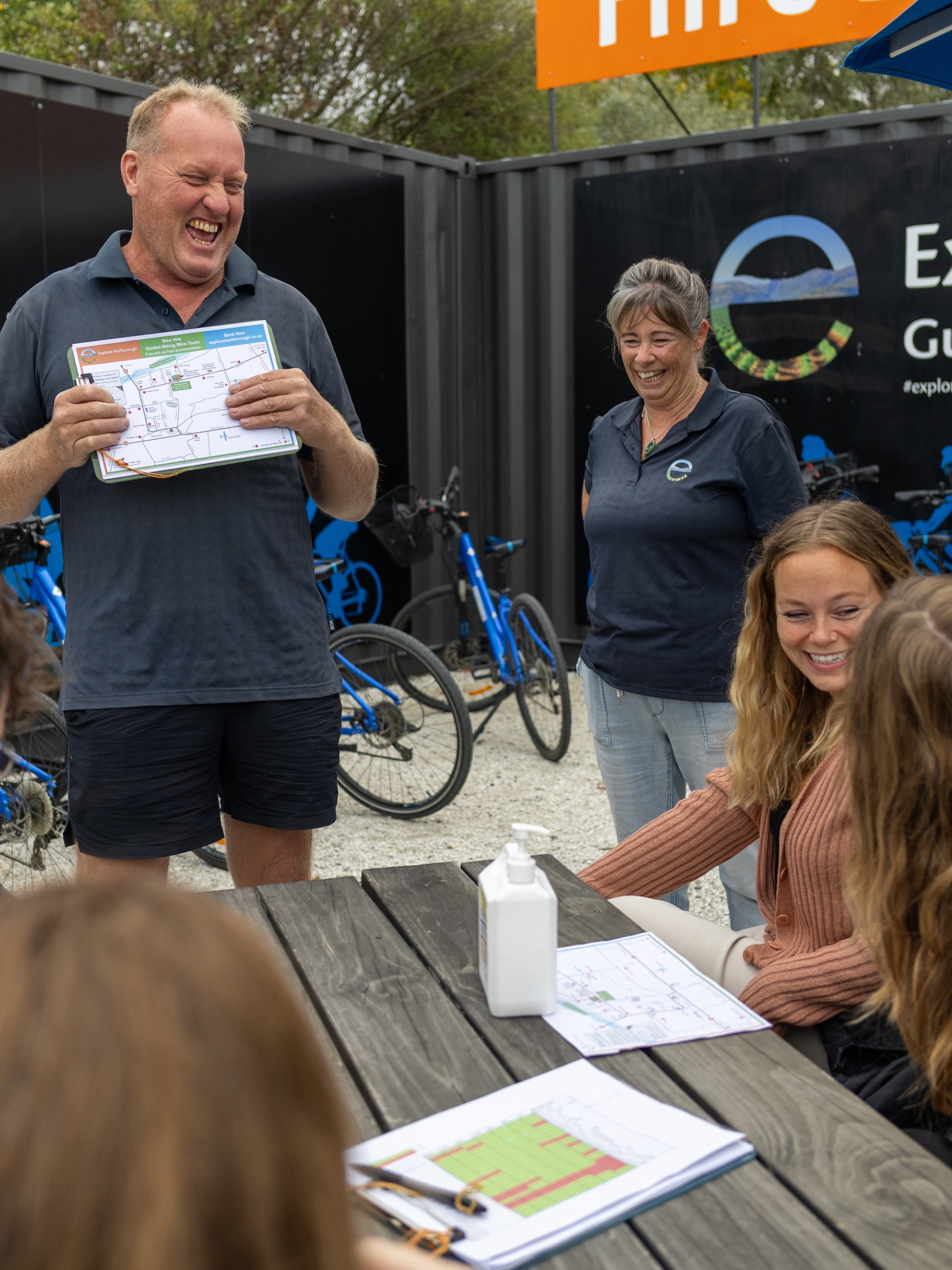 Man showing a map to smiling group by blue bikes and Explore Marlborough sign.