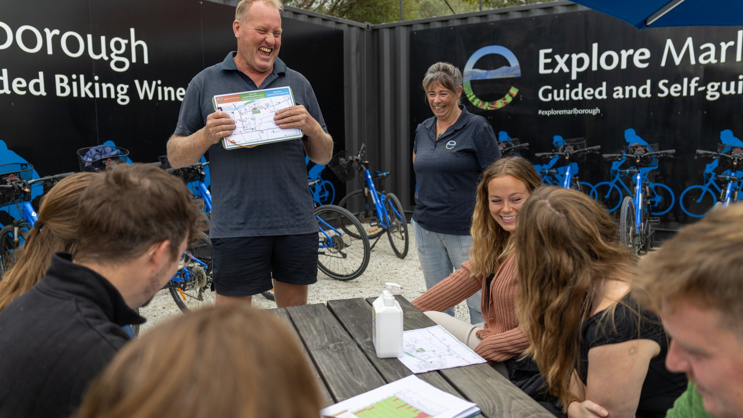 Man showing a map to smiling group by blue bikes and Explore Marlborough sign.