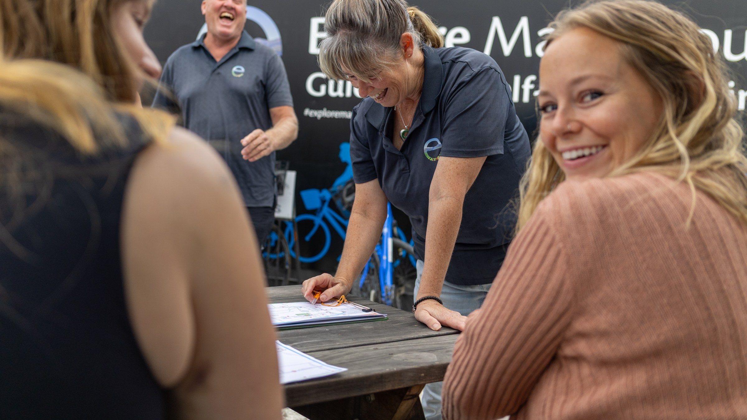 People laughing and smiling around a picnic table, one woman is writing on a paper.