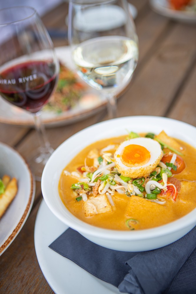 Bowl of curry with soft-boiled egg, vegetables, and tofu on a table with red and white wine glasses.