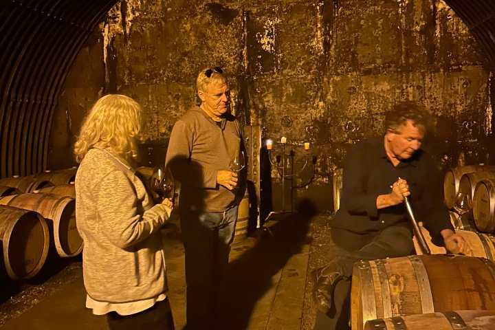 Three people tasting wine in a dimly lit barrel room.
