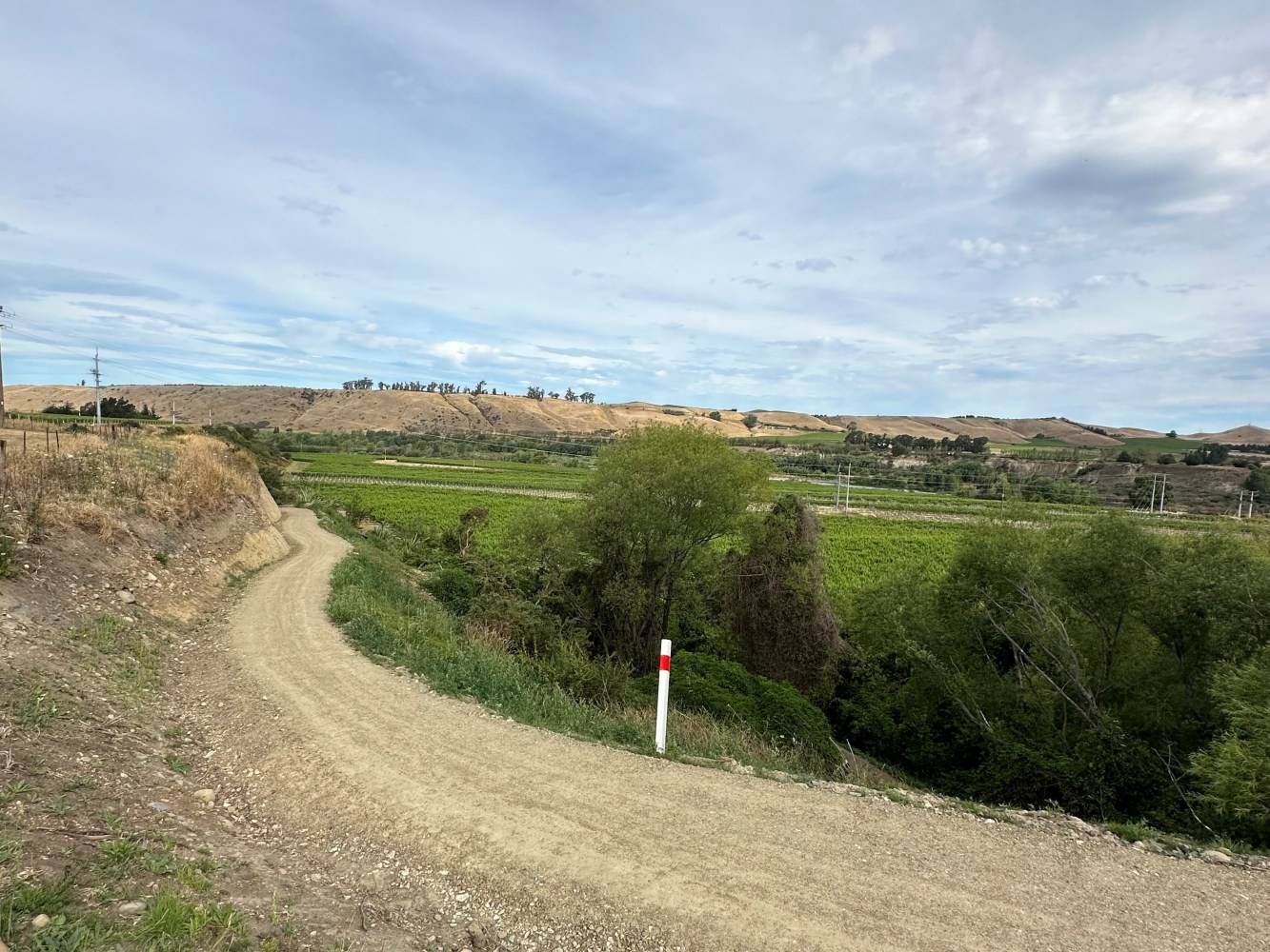 Dirt path winding through green fields under a cloudy sky with distant hills.