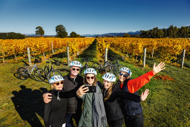 Group of people taking a selfie in a vineyard with bicycles and helmets.