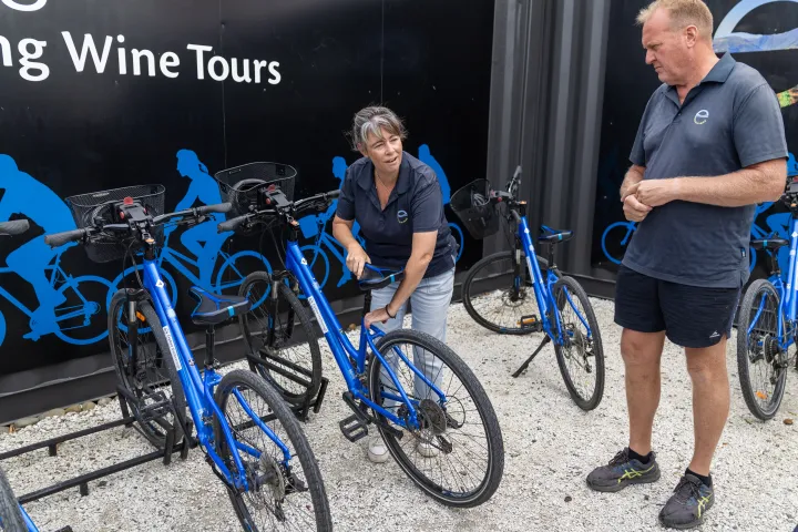 Two people in blue shirts inspecting blue bicycles near a 'Wine Tours' sign.