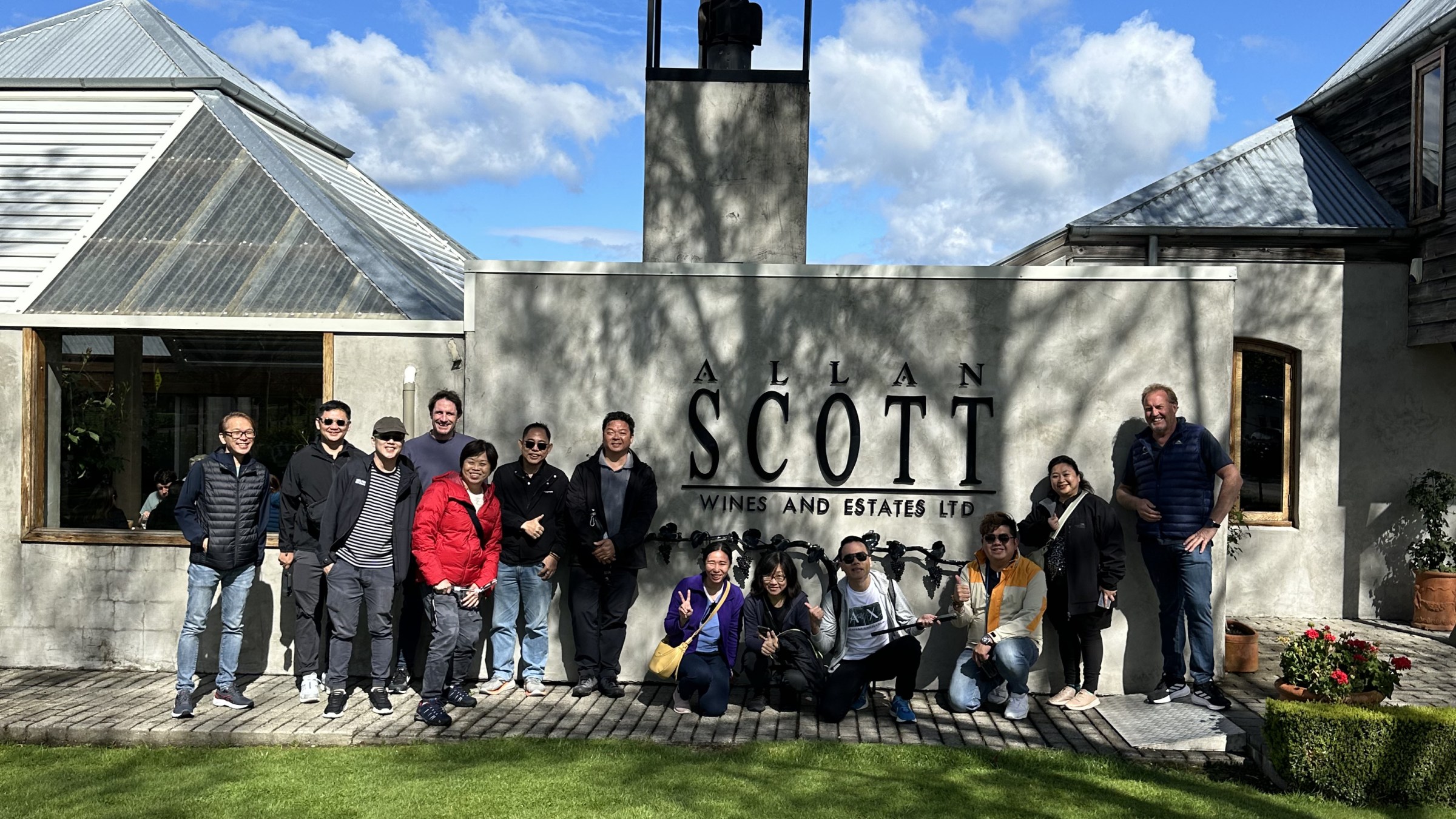 Group poses in front of Allan Scott Wines and Estates Ltd sign on a sunny day.