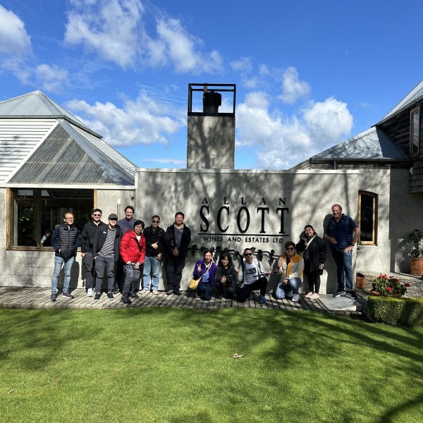 Group poses in front of Allan Scott Wines and Estates Ltd sign on a sunny day.