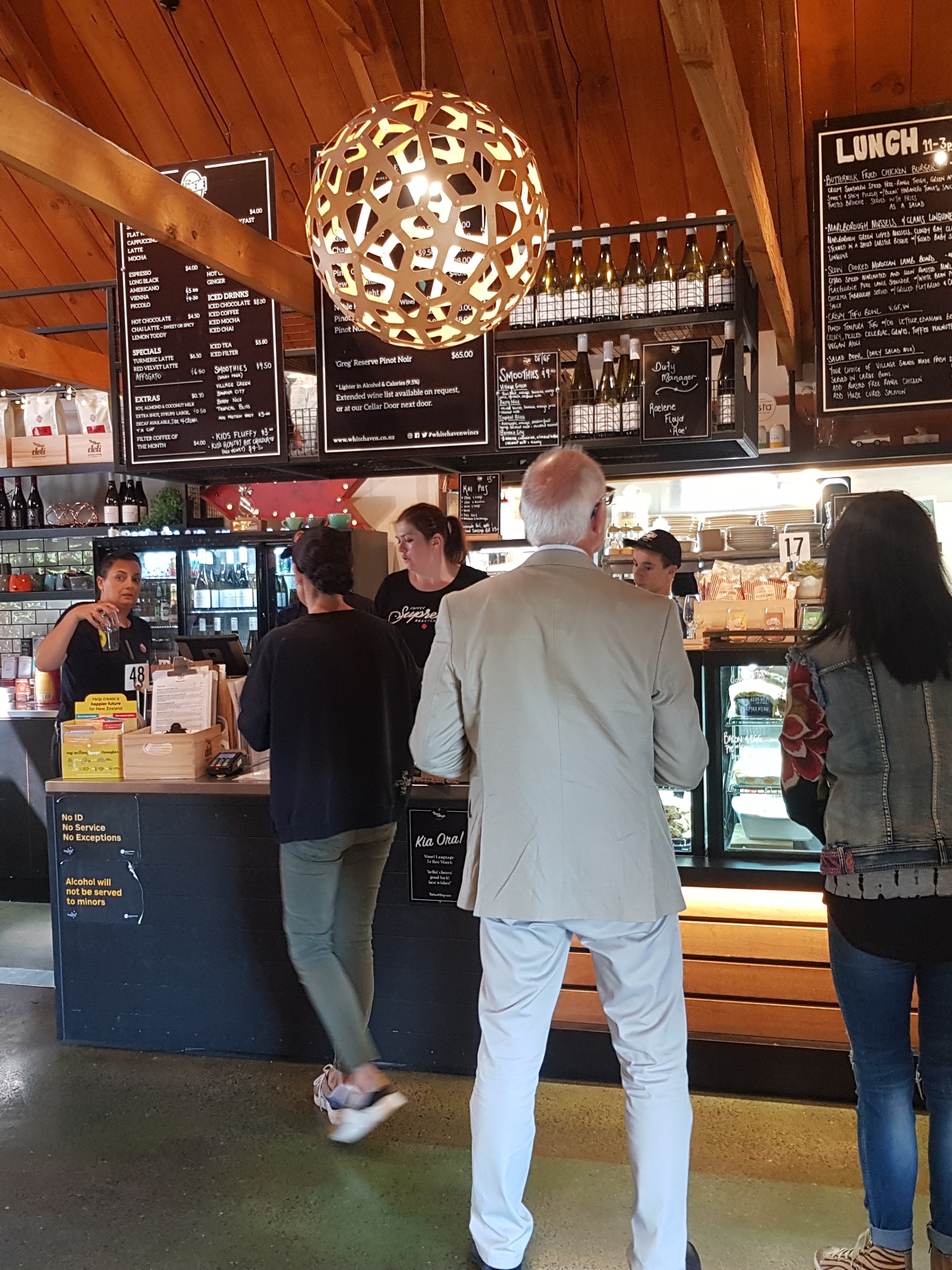 Cafe interior with wooden ceiling, people ordering at the counter.