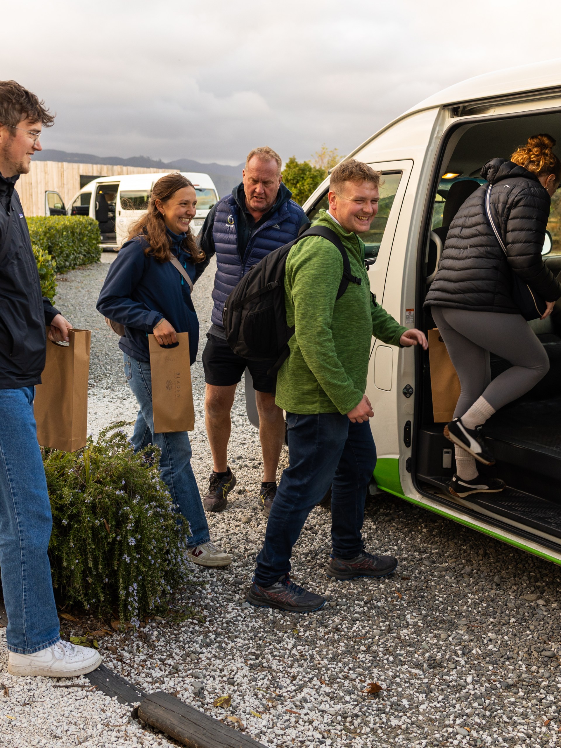 Group of people entering a white van with bicycles and bags on gravel.