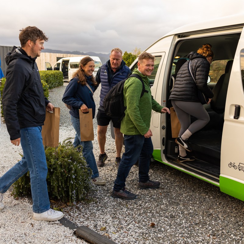 Group of people entering a white van with bicycles and bags on gravel.