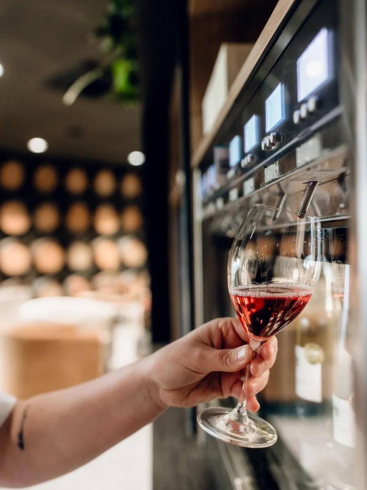 Person filling wine glass from a dispenser in a wine bar.