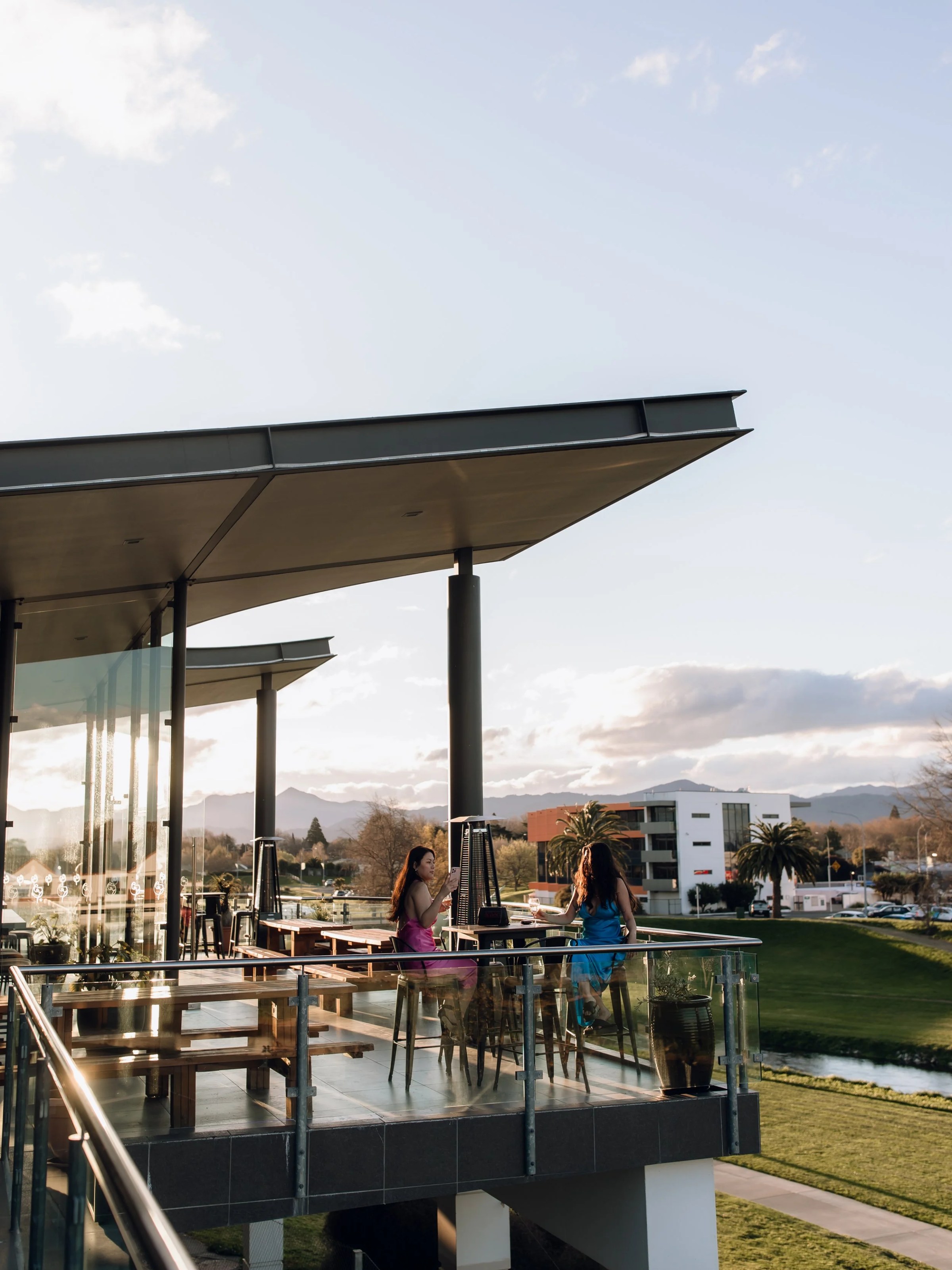 Two women on a modern outdoor patio with glass railing at sunset.