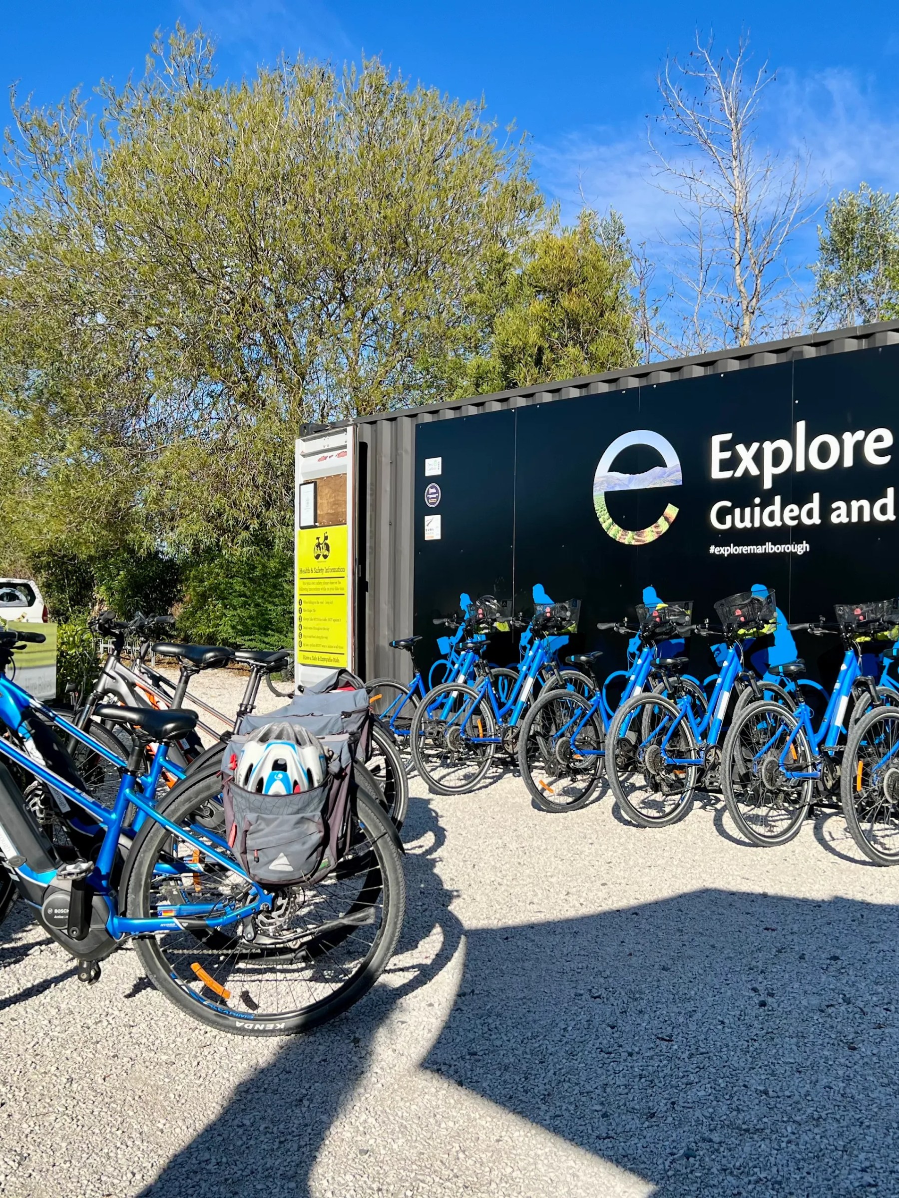 Blue bicycles lined up outside a rental shop with a black sign under a clear sky.