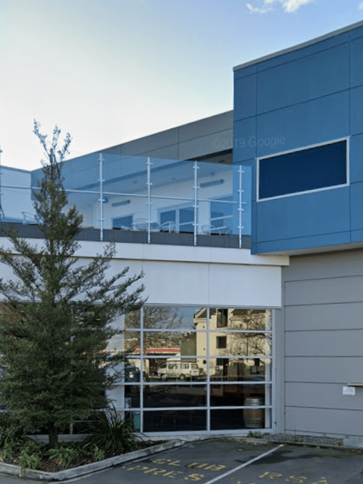 Modern building with blue-gray facade, large windows, and balcony with glass railing.