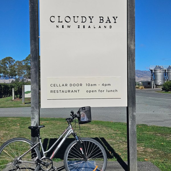 Bicycle parked in front of Cloudy Bay New Zealand sign under clear blue sky.