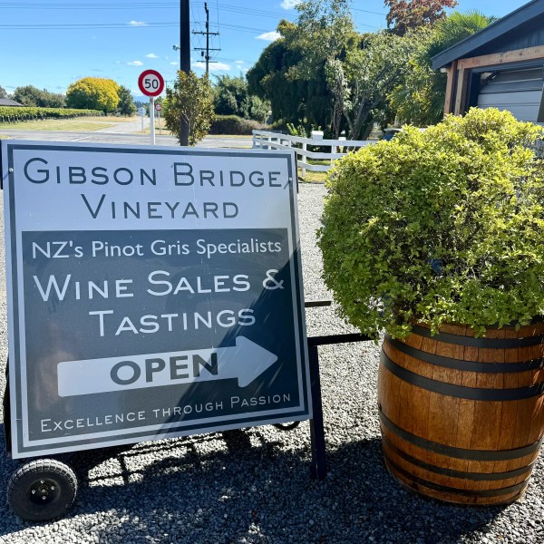 Sign reads 'Gibson Bridge Vineyard, Wine Sales & Tastings Open' next to a barrel with greenery.