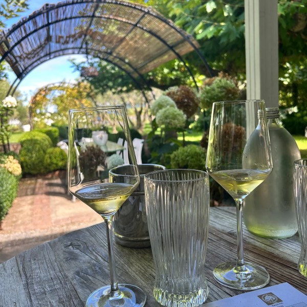 Two glasses of white wine on a table by a garden archway.