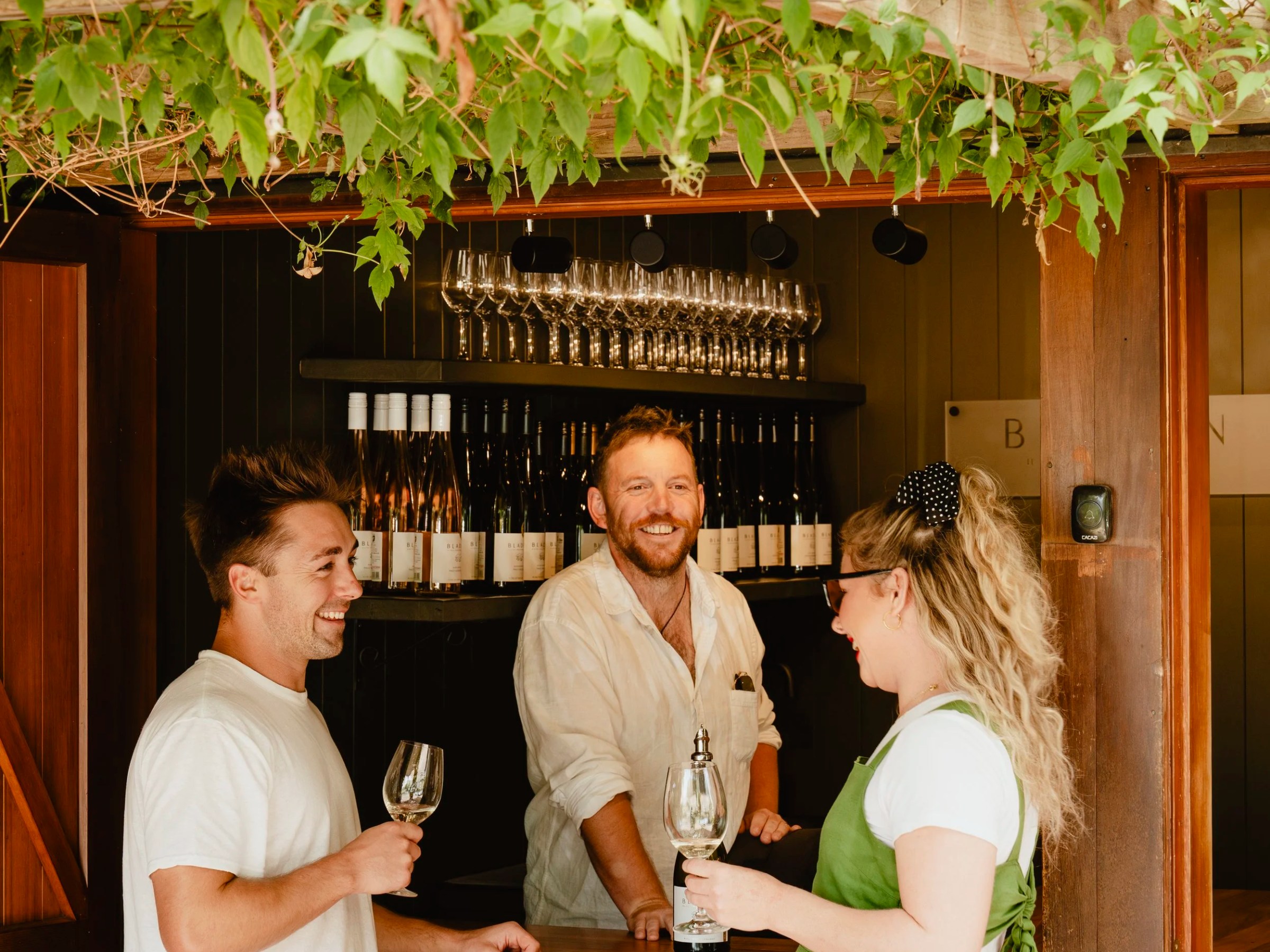 Three people enjoying wine tasting at a rustic outdoor bar.