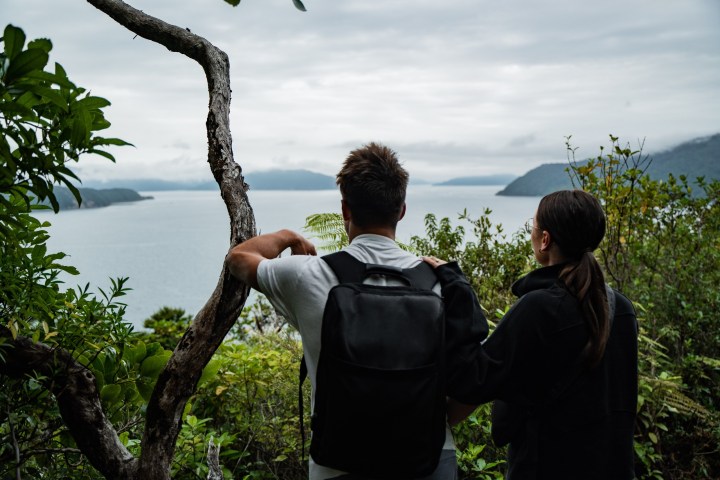 Two people with a backpack overlooking a lake surrounded by trees.