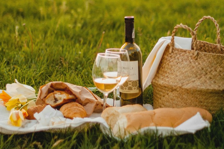 Picnic with wine, glasses, baguette, and pastries on grass.