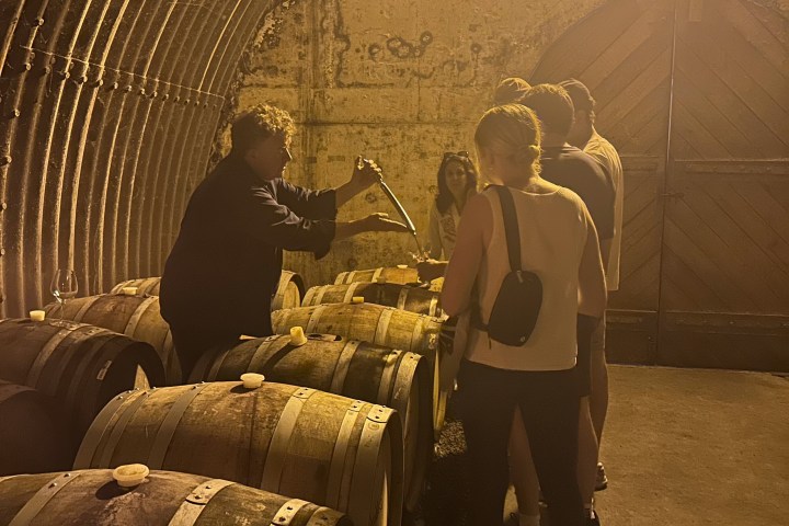 People in a dimly lit cellar tasting wine from barrels.