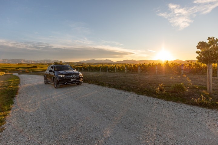 Car on dirt road by vineyard, sunset in the background.